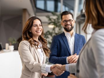 Two businesspeople smiling and shaking hands with a third person.