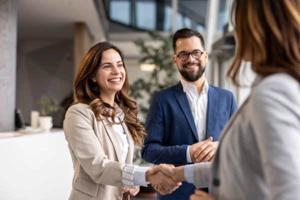 Two professionals shaking hands with a colleague, smiling warmly.