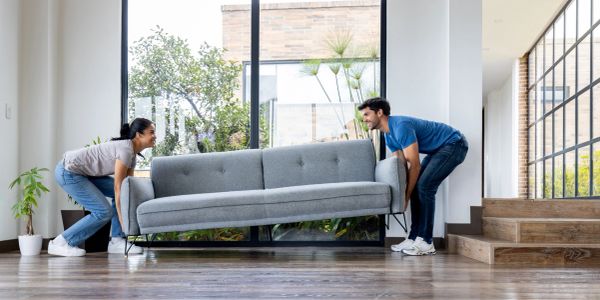 Couple lifting a gray couch inside a modern home.