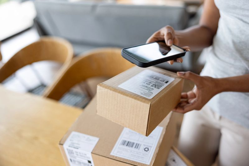 Close-up on a woman drop shipping a package from home using a mobile app on her cell phone