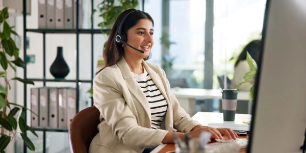 Woman working at a computer with a headset in an office.