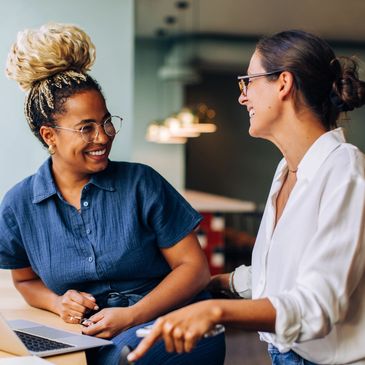 Two women smiling and chatting in a casual office setting.