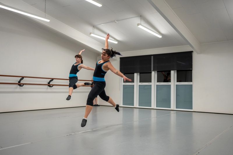 Two women are captured mid-air while rehearsing a choreographed dance routine in a modern studio.