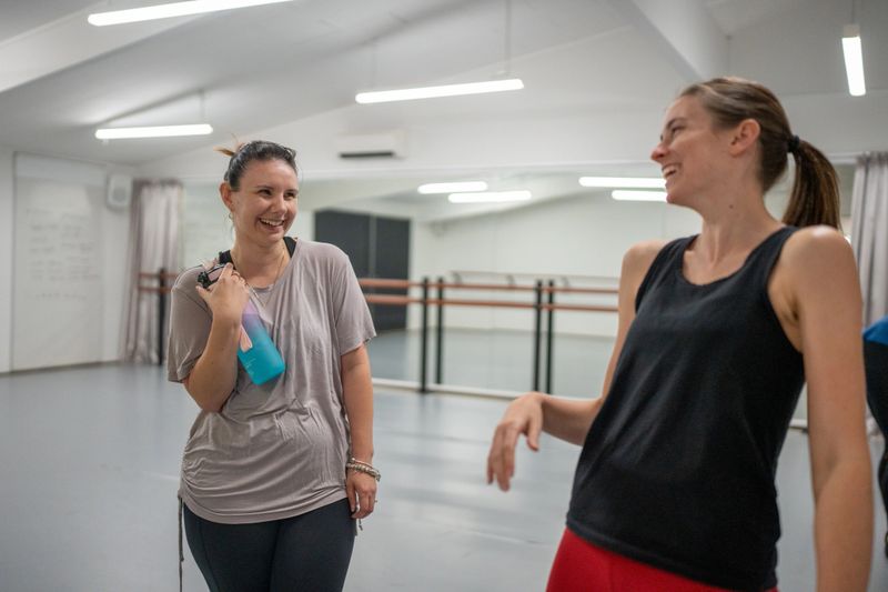 Two women laugh and chat together after a dance class in a modern studio.