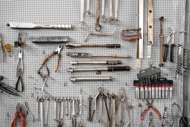 Various wrenches and hand tools hanging on pegboard in workshop. Neatly organized tools include combination wrenches, pliers, and adjustable wrenches for mechanical work