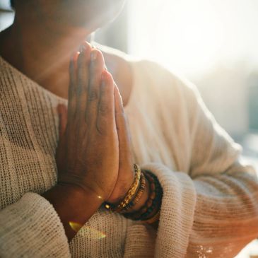 Person with hands in prayer gesture wearing bracelets and a sweater.