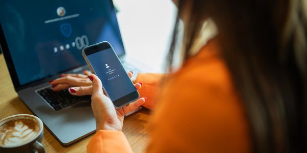 Woman using smartphone for two-factor authentication with laptop in background.