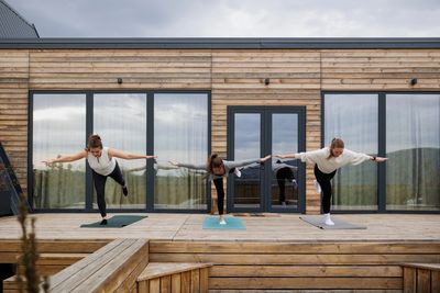 Three women practicing yoga balance poses outdoors on a wooden deck.