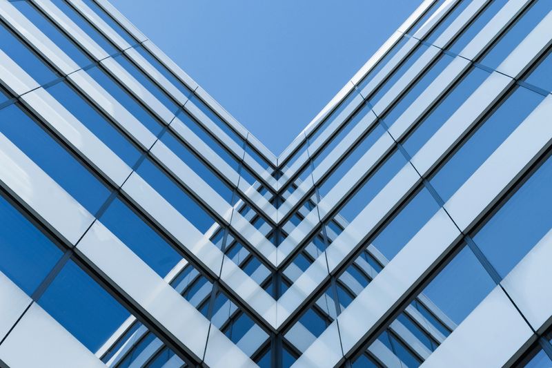 Photo shows a symmetrical view of a modern glass building facade with strong geometric lines. The image highlights architectural design and urban construction for use in business or real estate contexts.