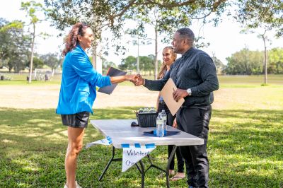 Volunteers shaking hands outdoors at a registration table.