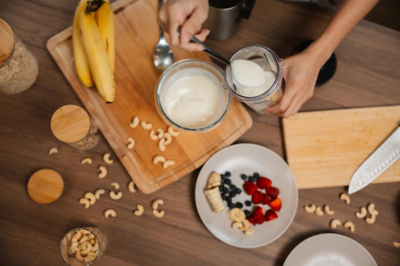 Close-up shot of woman adding creamy yogurt into a blender, preparing a healthy smoothie as part of her commitment to healthy living and nourishing her body with natural ingredients