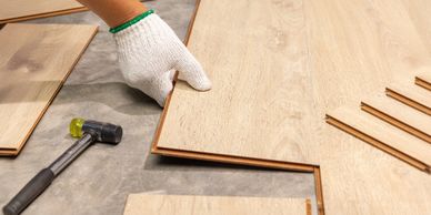 Hand installing wooden laminate flooring with tools nearby.