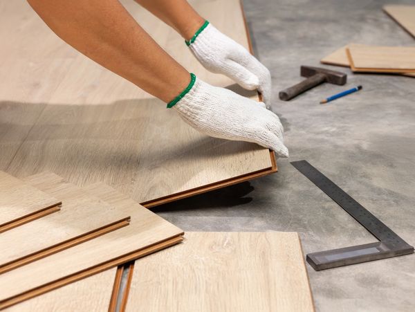 Person installing wood flooring with gloves and tools.