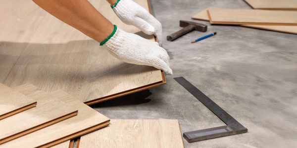 Person installing wooden flooring panels with gloves on.