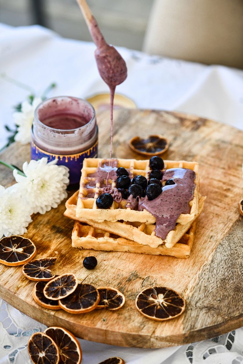 Female Generously Drizzling Colorful Blueberry Jam On Warm Golden Waffles During Cozy Morning Moment