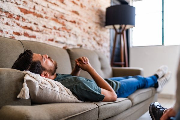 A man relaxing on a couch with hands clasped, eyes closed.