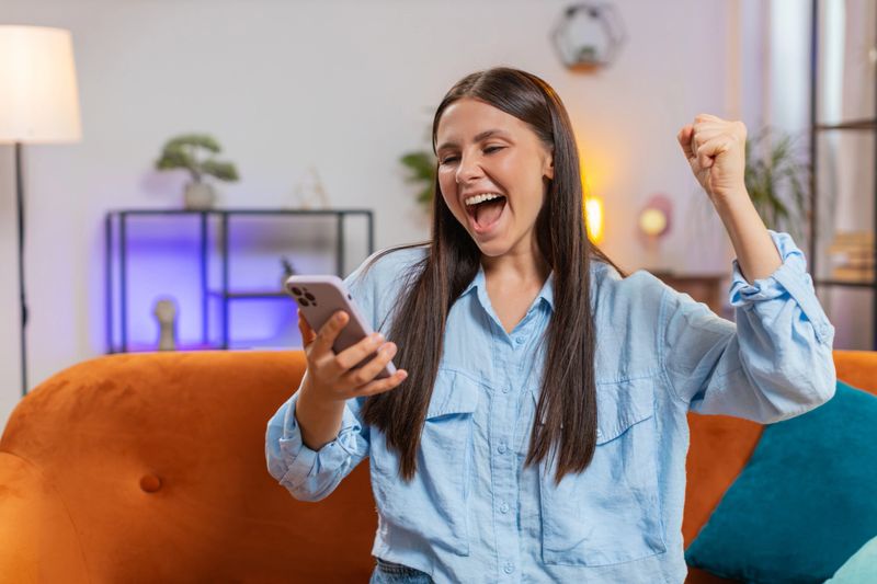 Surprised woman using mobile smartphone typing browsing say wow yes, celebrating success victory, winning lottery jackpot goal achievement play game good positive news, triumph. Girl at home on couch