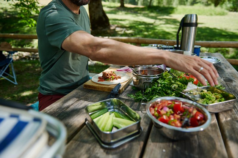 A scenic outdoor setup featuring a variety of colorful, fresh food items served on a wooden table, perfect for a peaceful picnic experience in natural surroundings.