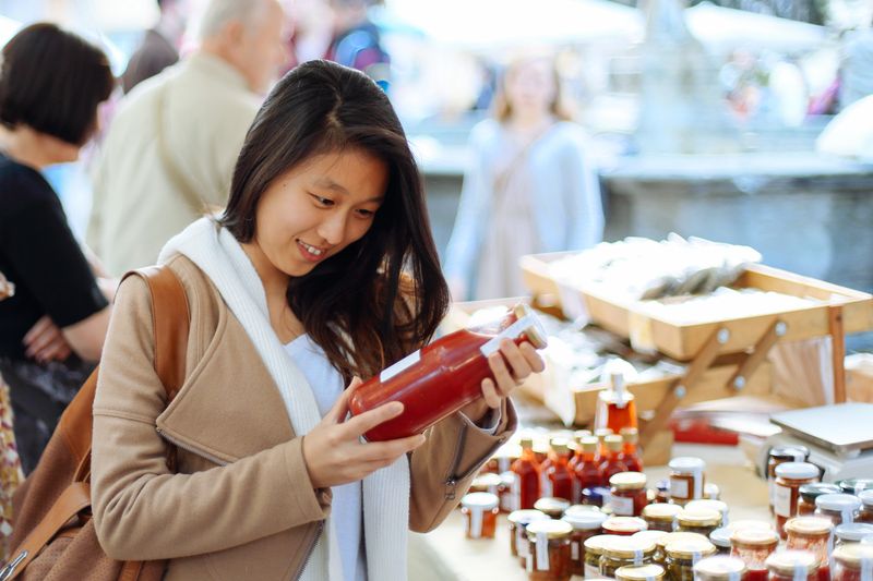 Young woman enjoys farmer's market in Florence during the weekend, Young lady checking the organic tomato sauce in Italian farmer's market, Florence.