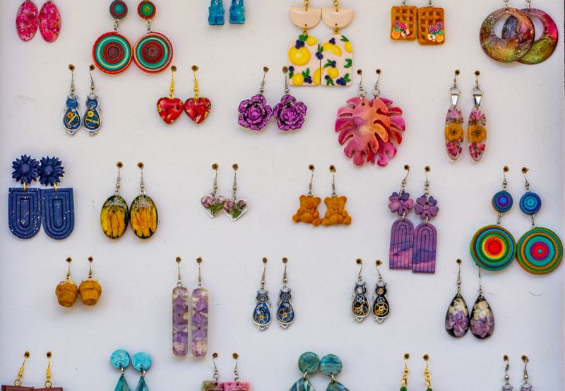 Colorful handmade earrings displayed on a white board at a craft market stall.