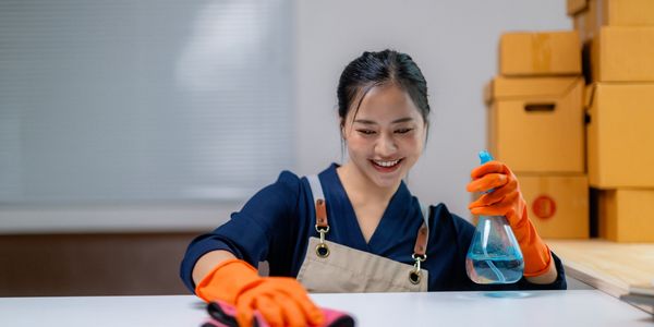Woman in orange gloves cleaning a surface with a spray bottle and cloth.