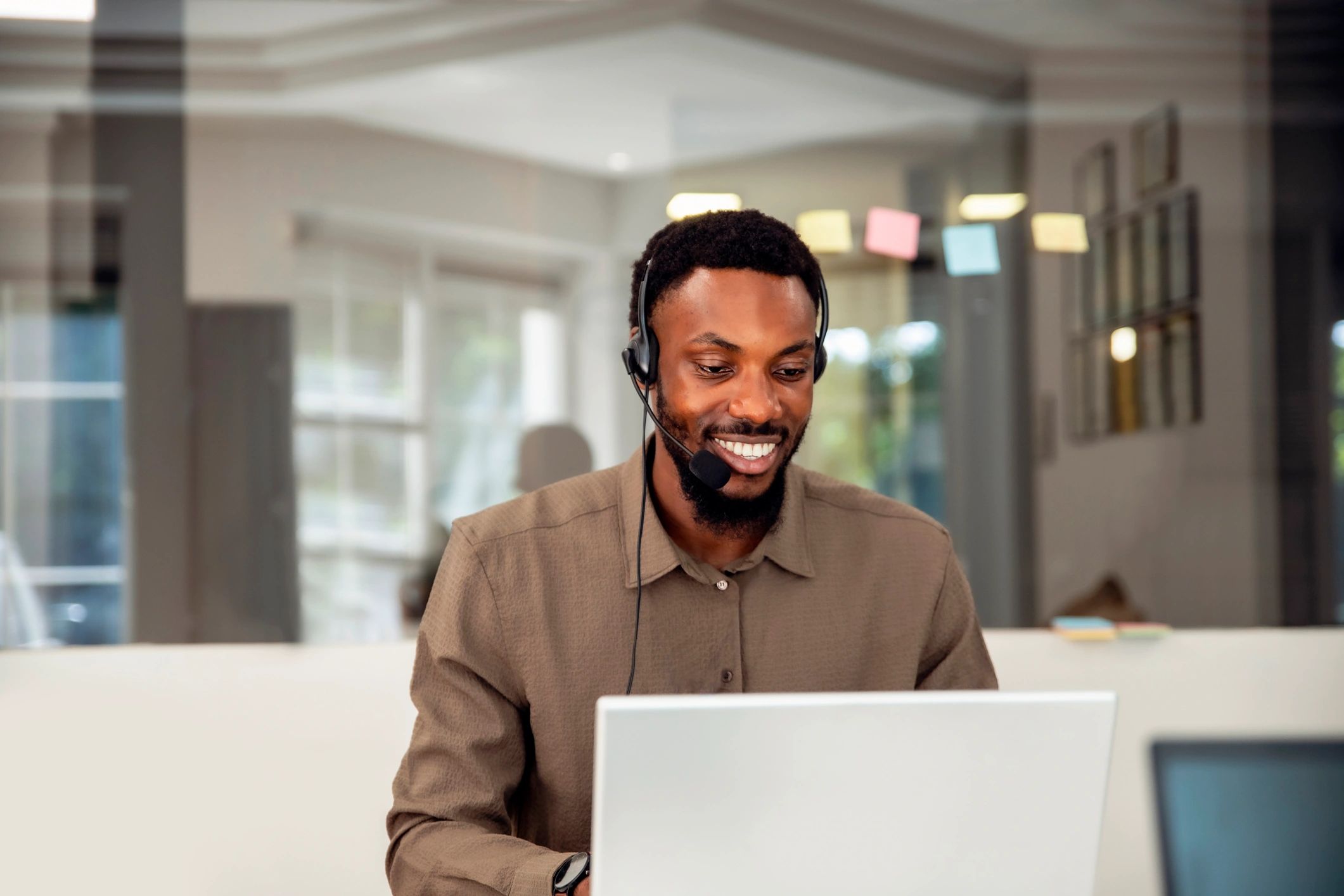 Smiling man wearing headset working on laptop.