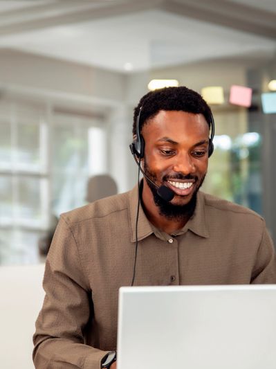 Smiling man wearing a headset working on a laptop.
