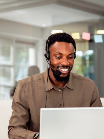 Man wearing headset smiling while working on laptop.