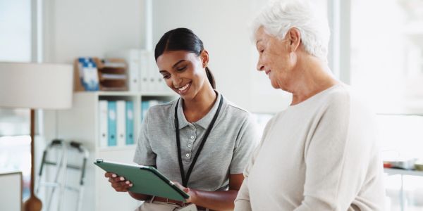 Young nurse assisting elderly woman with tablet.