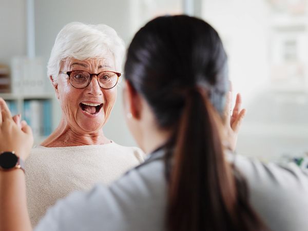 Older woman joyfully high-fiving a younger woman in a bright room.