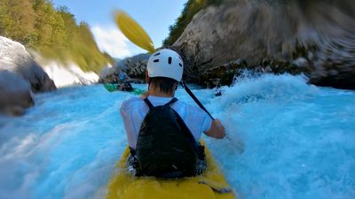 Kayaker navigating through rough whitewater rapids in a scenic river canyon.