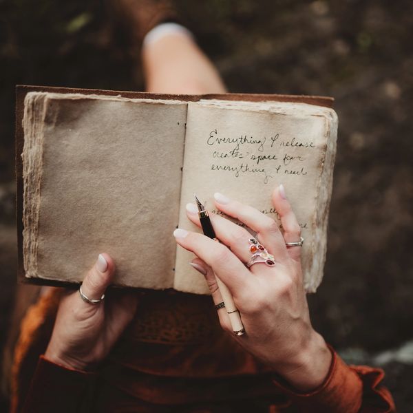 Person holding an old journal, writing with a fountain pen.