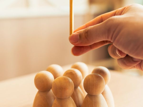 Hand placing a wooden stick among wooden peg figures on a table.