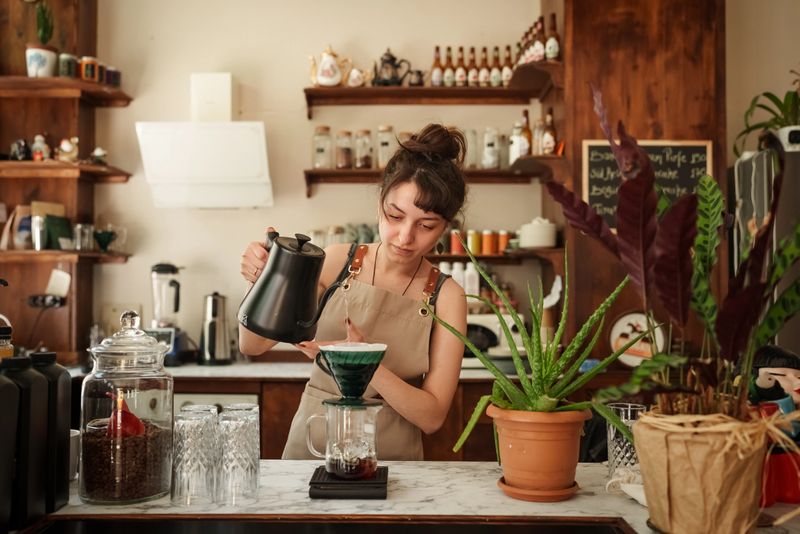 A young barista carefully pours hot water over ground coffee using the pour-over method in a warm, rustic café. The scene highlights slow coffee culture, craftsmanship, and attention to detail.