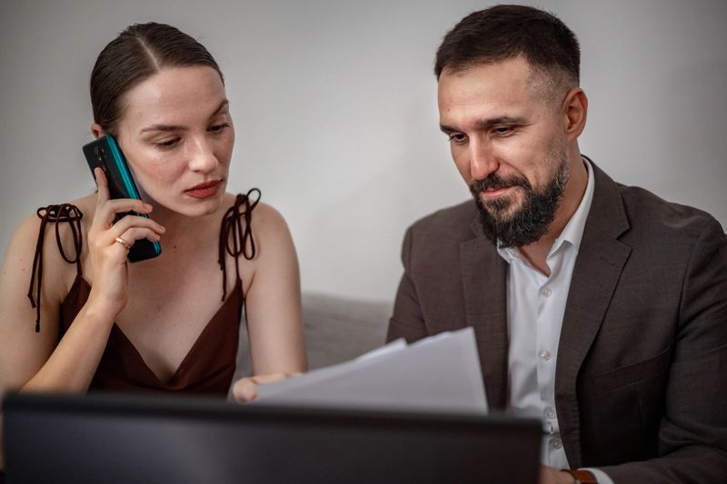 In a dynamic office setting, a female employee provides real-time updates over the phone to her teammate, who is focused on reviewing key business documentation