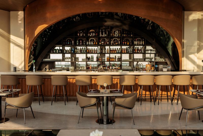Straight-on view of a sleek, modern bar counter with stylish bar stools and neatly arranged tables in front. In Bangkok, Thailand.