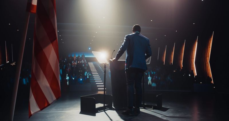 Political Party Representative Speaking at a Press Conference in Government Building. Press Officer Delivering a Speech at a Summit. Minister Talking at Congress. Stage with American Flags