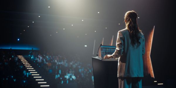 Woman speaking at a podium in front of a large audience.