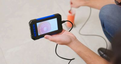 Person holding an inspection camera showing a pipe interior on the screen.