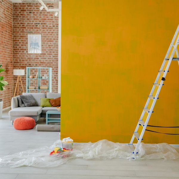 Ladder and painting supplies in a living room with a yellow accent wall.