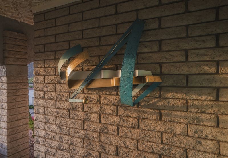 Colorful mid-century metal wall art mounted on vintage brick exterior, capturing retro textures and sculptural shadows in the afternoon light.