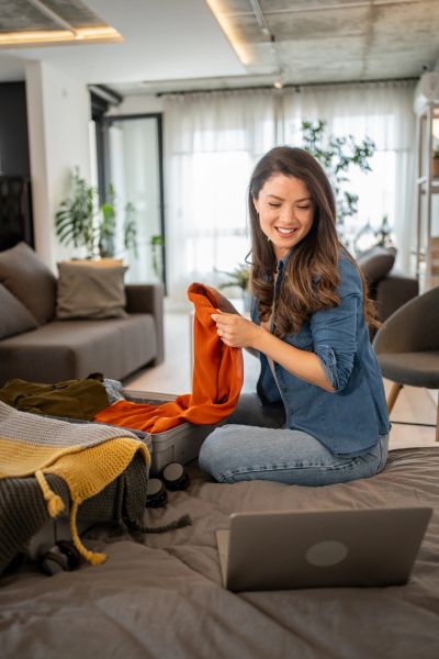 Woman packing an orange sweater into a suitcase at home.