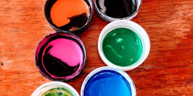 Open paint containers with different colors on a wooden surface.
