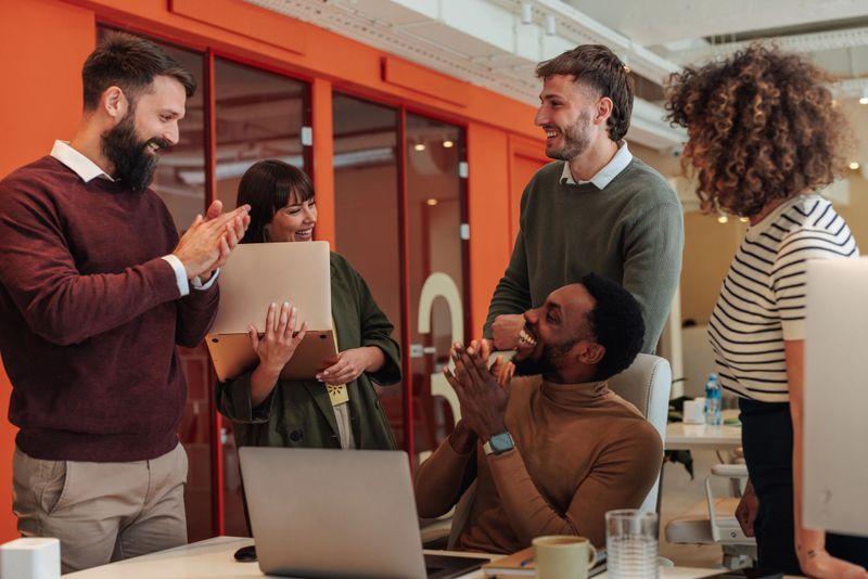 Diverse colleagues clapping, laughing, and enjoying a successful moment together in a vibrant office space