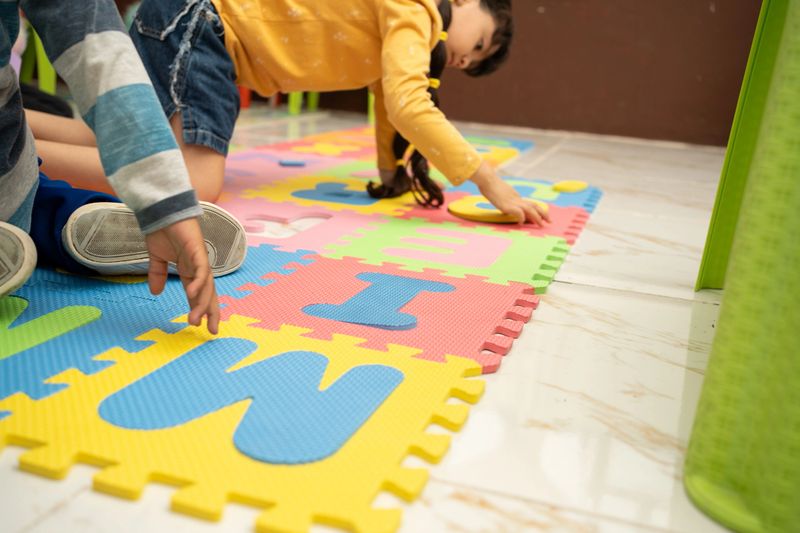 Children placing foam letters into a colorful alphabet puzzle mat on the floor. Preschool literacy activity supports letter recognition and fine motor skill development in kindergarten