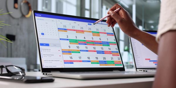 A person uses a stylus to interact with a colorful calendar on a laptop.