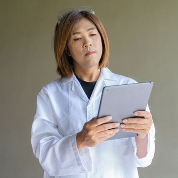 Scientist in a white lab coat examining a tablet.