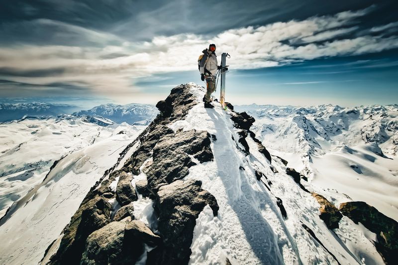 Backcountry skier on mountain top at sunset, glaciated mountains around him, Saas-Fee, Swiss Alps