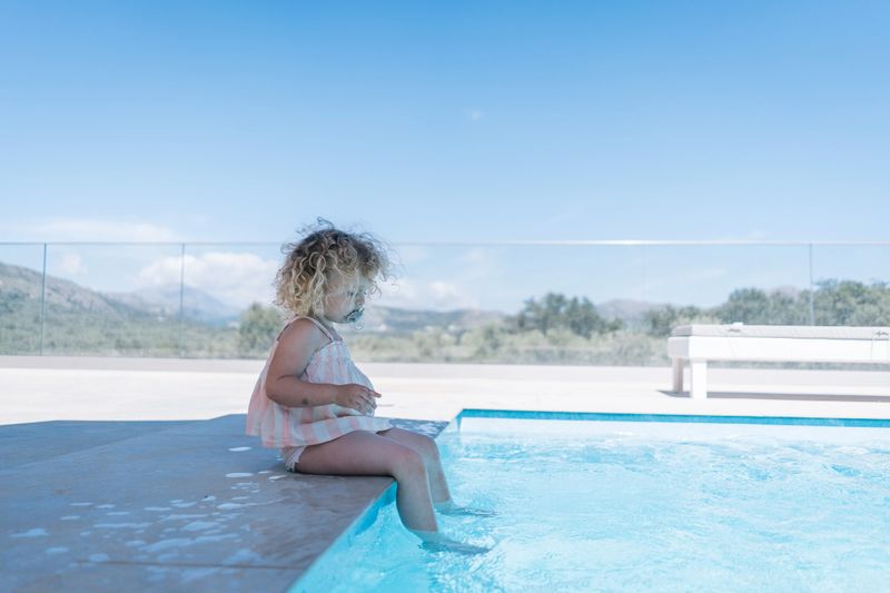 Baby girl sits on edge of swimming pool, Crete
