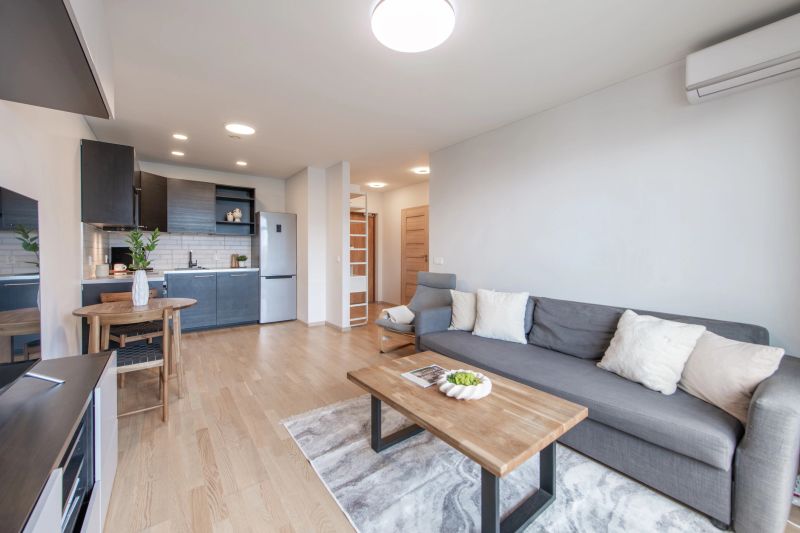 View of a modern open-plan living room and kitchen featuring stylish furniture, wooden flooring, and soft lighting.